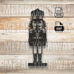 Op de afbeelding: Zwarte metalen uitsnede van een notenkrakersoldaat met een kroon, snor en uniform. De afbeelding bevat SVG- en DXF-bestandspictogrammen. De achtergrond is een lichtbruin houten oppervlak met de tekst "METAL YOUR WAY" herhaald.