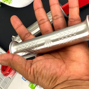 May include: A close-up of a silver rolling pin with a criss-cross pattern and a small bear design. The rolling pin is held in a hand.