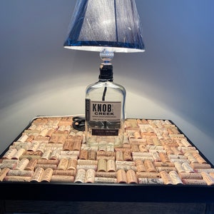 May include: A table lamp made from a Knob Creek bourbon bottle with a black lampshade. The table top is covered in a mosaic of wine corks.