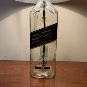 Puede incluir: Una botella de vidrio transparente con una etiqueta negra que dice "JOHNNIE WALKER BLACK LABEL BLENDED SCOTCH WHISKY John Walker & Sons" y una etiqueta dorada que dice "AGED 12 YEARS".