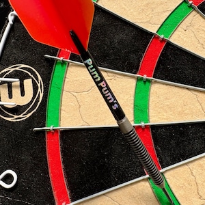 May include: A dart with a red flight is embedded in a dartboard. The dart has a black shaft with the text "Pum Pum's". The dartboard is black with red and green sections.