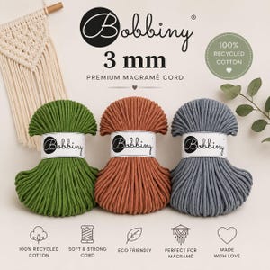 Könnte beinhalten: Drei Garnknäuel aus 3 mm Bobbiny Premium-Makramee-Kordel in Grün, Terrakotta und Grau. Jedes Knäuel hat eine weiße Papierbanderole mit dem Bobbiny-Logo. Das Bild enthält Text mit Angaben zu 100% recycelter Baumwolle sowie weicher und starker Kordel.