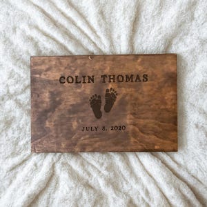 May include: A wooden plaque with the name "Colin Thomas" and the date "July 8, 2020" engraved on it. Two small footprints are also engraved on the plaque.