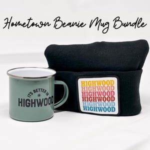 May include: A green enamel mug with the text "It's Better In Highwood" and a black beanie with a colorful patch that reads "Highwood" repeated multiple times. The mug and beanie are part of a hometown bundle.