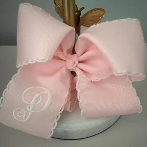 May include: A large pink bow with white scalloped edges and a white embroidered letter "P" in the center.