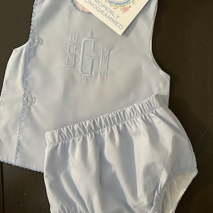 Puede incluir: Conjunto de ropa de beb&eacute; azul claro, que incluye una parte superior con iniciales bordadas y bragas a juego. La parte superior tiene cierres de bot&oacute;n y un borde festoneado. La etiqueta dice "PROPERLY MONOGRAMMED".