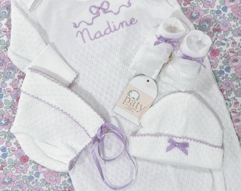 May include: A white knitted baby gown with a lavender bow and the name "Maddie" embroidered on the front. The set includes a matching hat, booties, and headband.