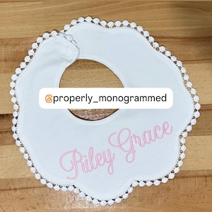 May include: White baby bib with a scalloped edge and a pink embroidered name "Riley Grace".