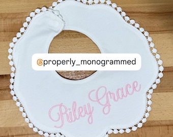May include: White baby bib with a scalloped edge and a pink embroidered name "Riley Grace".
