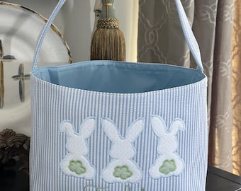 Puede incluir: Cesta de Pascua a rayas azules y blancas con tres conejos bordados y el nombre "Fielder" en hilo verde.