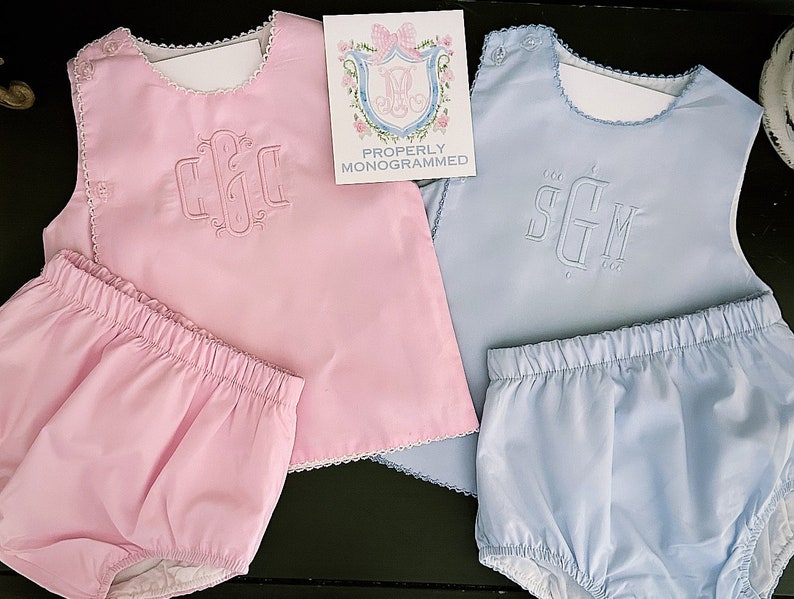 Puede incluir: Dos conjuntos de ropa de beb&eacute;: uno rosa y otro azul claro. Cada conjunto incluye una camiseta sin mangas con iniciales bordadas y bragas a juego. Las camisetas tienen bordes festoneados y se combinan con bragas. Una tarjeta dice "Properly Monogrammed".