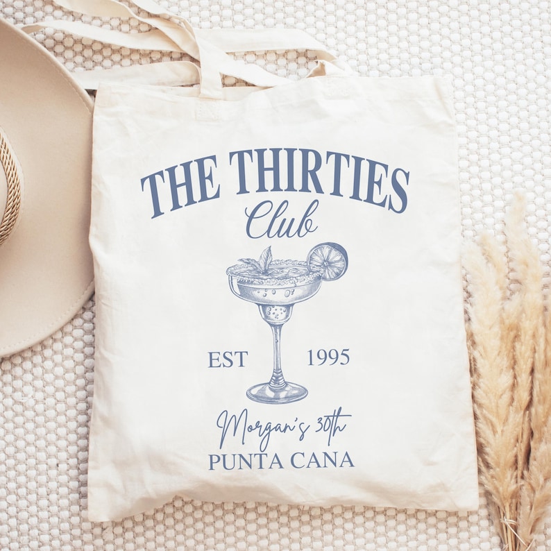 Peut inclure: Sac fourre-tout cr&egrave;me avec texte bleu et illustration de margarita. Le texte indique "THE THIRTIES Club" au-dessus d'un dessin de verre &agrave; margarita, avec "EST 1995" et "Morgan's 30th PUNTA CANA" en dessous. Le sac a une conception simple de poign&eacute;e.