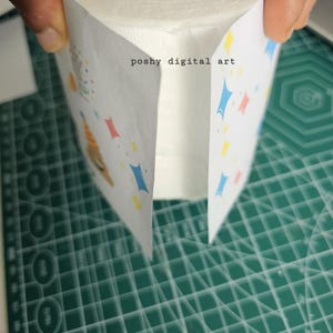 May include: A roll of white toilet paper with a colorful design on the outside. The design features blue, red, and yellow shapes and the text "poshy digital art".