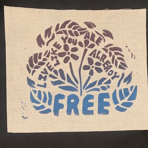 May include: A beige fabric wall hanging with a blue and purple floral design. The flowers are surrounded by the words "Like You Are Already Free".