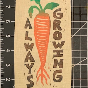 May include: A brown fabric print with a large orange carrot and the text "ALWAYS GROWING" in brown lettering.