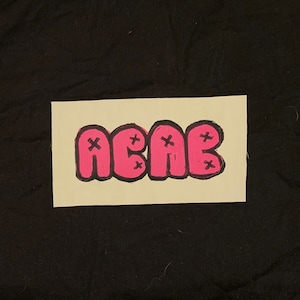 May include: A pink sticker with the word "ACAE" written in black outlined bubble letters. Each letter has an "X" drawn on it.