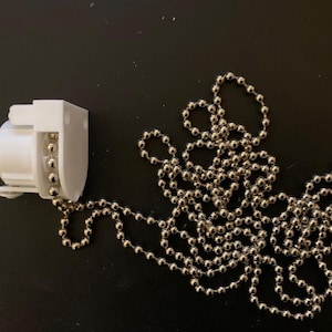 May include: White plastic blind lift mechanism with a silver beaded chain.