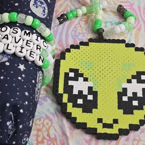 May include: A selection of handmade rave accessories. Features a beaded alien pendant and several bracelets with green and white beads. One bracelet spells out "COSMIC RAVER ALIEN" in white letter beads.