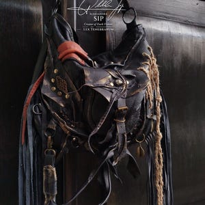 May include: Black leather shoulder bag with detailed embellishments, including buckles, fringe, and metal accents. The bag has a distressed, textured look with dark brown and gold tones, and a long strap.