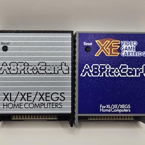May include: Two rectangular video game cartridges for XL/XE/XEGS home computers. The left cartridge is black with a silver faceplate labeled A8PicoCart. The right cartridge is gray with a blue faceplate labeled XE Video Game Cartridge A8PicoCart.