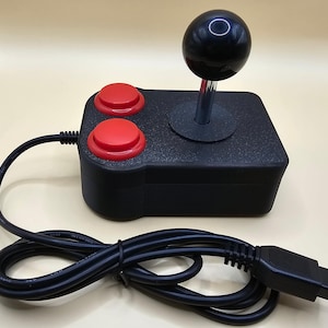 Pode incluir: Um joystick preto com um botão vermelho e um cabo preto. O joystick tem uma bola preta no topo e uma base preta.