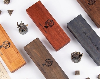 May include: Four rectangular wooden boxes in varying shades of brown, each featuring a laser-engraved 20-sided die graphic and the text YOUR TEXT HERE. The boxes are surrounded by metal miniature figurines, polyhedral dice, gold coins, and a pen.