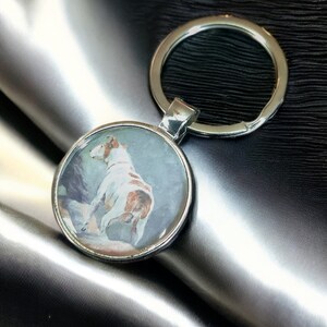 May include: A silver key chain with a round, clear glass charm featuring a watercolour painting of a white and brown dog.