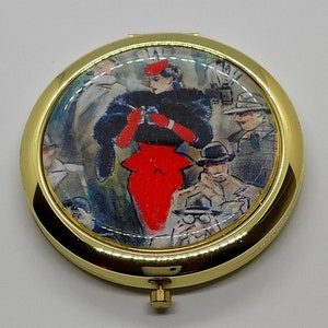 Peut inclure: Un miroir compact doré avec une illustration vintage d'une femme en robe rouge et manteau en fourrure noire. La femme est entourée d'autres personnes dans l'illustration.