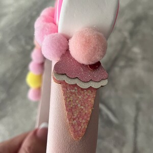 May include: Pink headband with a pink and white ice cream cone charm, pink pom poms, and a white marshmallow charm.
