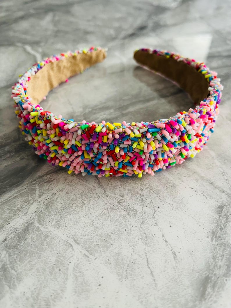 May include: A headband with a brown base covered in colourful sprinkles. The sprinkles are pink, blue, green, yellow, and white.