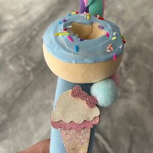 May include: A blue and white donut with colorful sprinkles, a blue and white ice cream cone with pink glitter, and a blue and white pom-pom on a blue fabric headband.