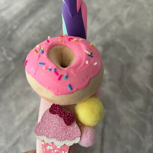 May include: Pink headband with a pink donut, a pink ice cream cone with a pink bow, and a yellow pom-pom.
