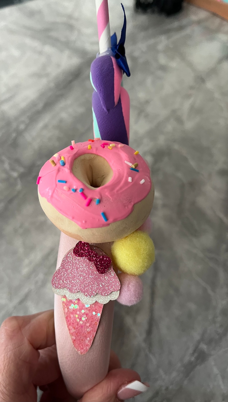 May include: Pink headband with a pink donut, a pink ice cream cone with a pink bow, and a yellow pom-pom.