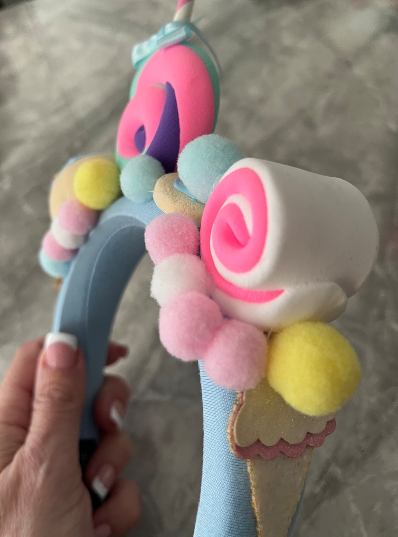 May include: A blue headband with a variety of colorful decorations, including pink and white swirl candies, pastel pom-poms, and a light blue and pink ice cream cone.