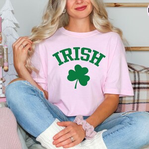 a woman sitting on a couch wearing a pink shirt with a shamrock on it