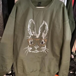 A green sweatshirt with a white illustration of a rabbit wearing glasses.