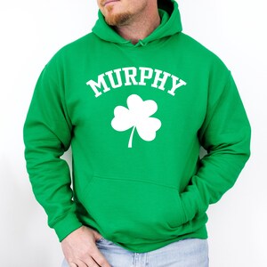 A man wearing a green hoodie with the word 'MURPHY' printed on it, along with a white clover symbol.