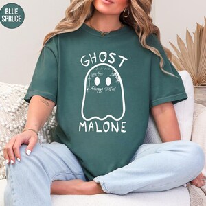 A woman wearing a green t-shirt with a ghost design and the text "GHOST MALONE" is sitting on a couch.
