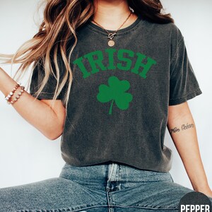 a woman sitting on the ground wearing a shirt with a shamrock on it