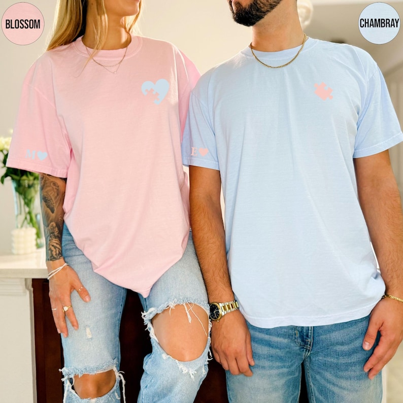 A man and a woman wearing matching t-shirts with a heart design stand together.