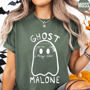 A woman wearing a green t-shirt with a graphic of a ghost and the text "GHOST MALONE" printed on it.