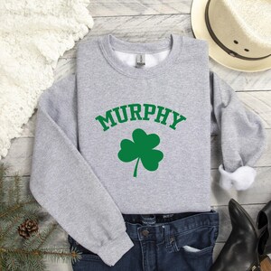a casual outfit consisting of a gray sweatshirt with the word "MURPHY" printed on it, a pair of jeans, and a hat.