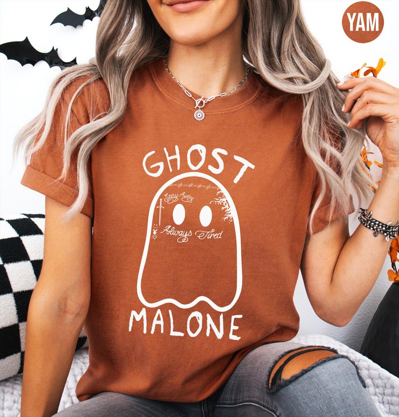 A woman wearing a brown t-shirt with a ghost graphic and the text "GHOST MALONE" is sitting on a couch.