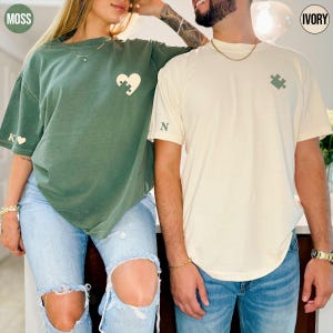 A man and a woman standing close together, both wearing t-shirts with a heart design.