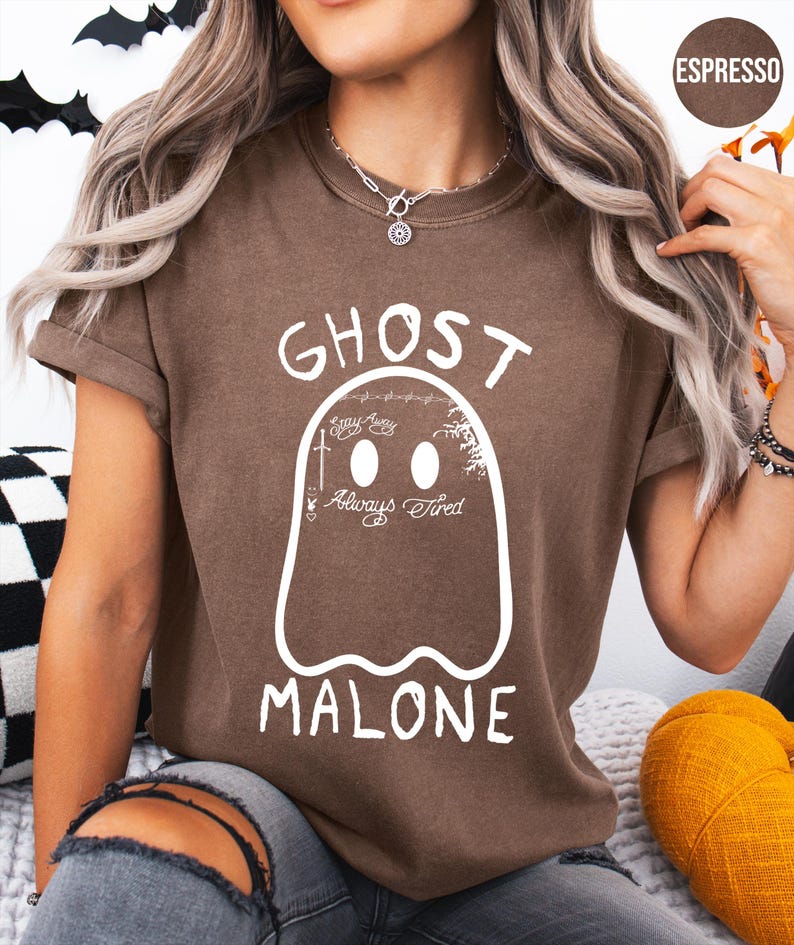 A woman wearing a brown t-shirt with a ghost design and the text "GHOST MALONE" printed on it.