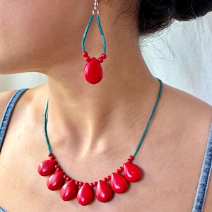 May include: A red teardrop-shaped jewelry set, including a necklace and earrings. The necklace features seven red teardrop pendants connected by a teal cord. The earrings have a similar design, with a single red teardrop pendant and teal accents.