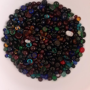 May include: A bowl filled with a variety of small, round glass beads in shades of black, brown, red, green, and blue.