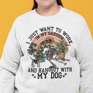 May include: A gray sweatshirt with a graphic print of a skeleton gardening with a dog. The text reads "I just want to work in my garden and hangout with my dog".