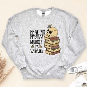 May include: Gray sweatshirt with a skull and stack of books. The text reads "Reading because murder is wrong".