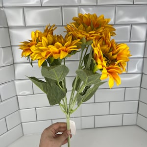 May include: A bouquet of artificial sunflowers with green leaves. The sunflowers are yellow with brown centers.